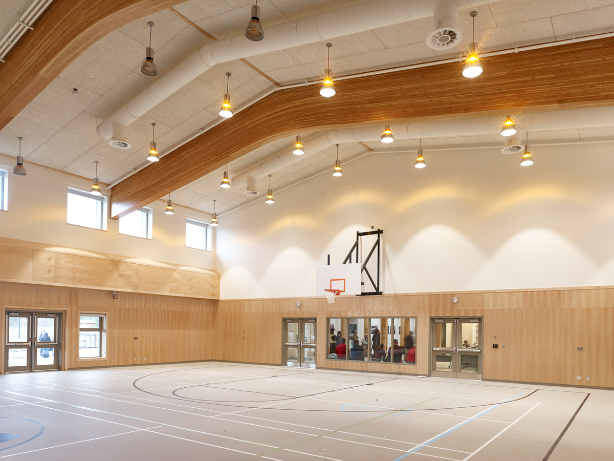 Interior daytime view of Nadleh Whutenne Yah Administration and Cultural Building gymnasium showing glue-laminated timber (glulam) above wood paneled walls with extensive millwork throughout