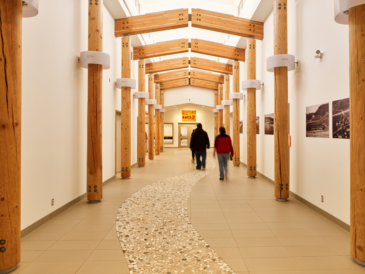 Interior daytime view of Nadleh Whutenne Yah Administration and Cultural Building central hallway showing glue-laminated timber (glulam) beams above and wood pole columns