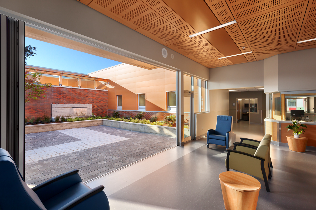 Interior outward view of Nanaimo Regional General Hospital Emergency Department entrance area, showing large open entrance, exterior courtyard, and extensive use of wood, including wood ceiling paneling on the building interior