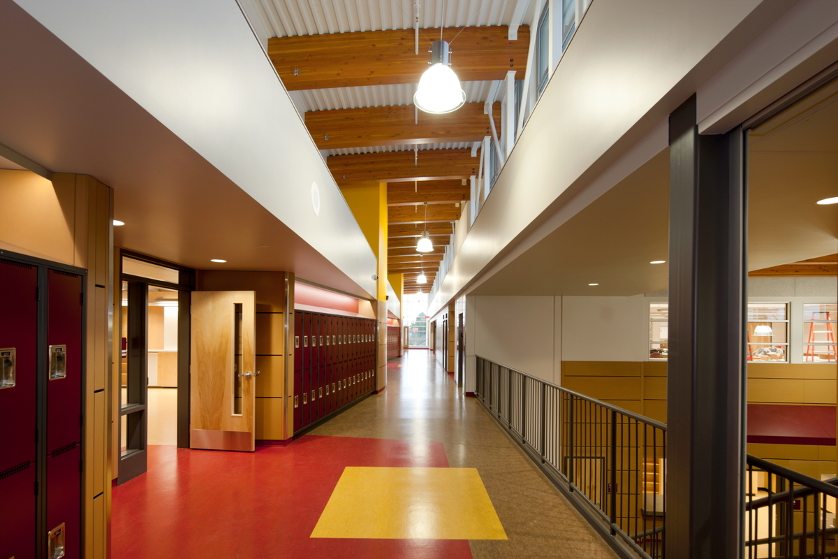 Interior view of North Saanich Middle School multi-storey main hall, showing hybrid metal, wood and concrete construction and including solid mass timber paneling, post + beam, and glue-laminated timber (Glulam) beams