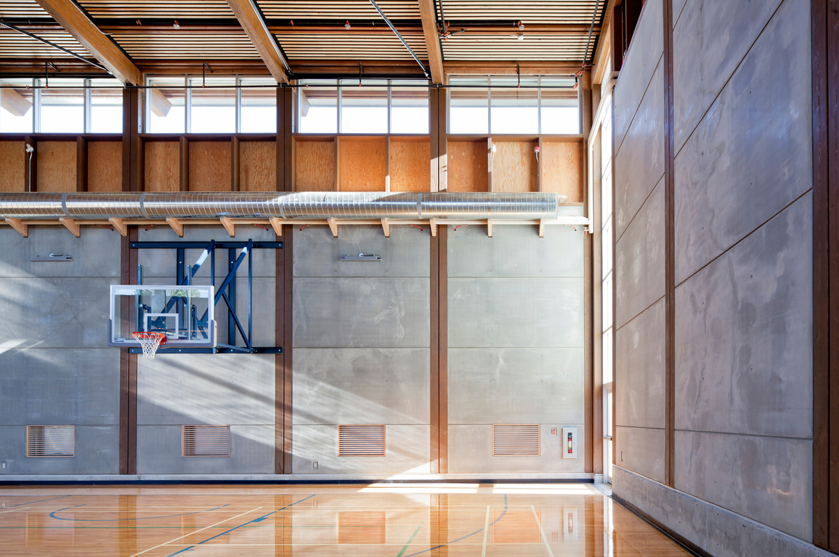 Interior sunny daytime view of low rise Okanagan College gymnasium showing hybrid construction with light frame and mass timber construction, including cross-laminated timber (CLT), laminated veneer lumber (LVL) and prefabricated elements