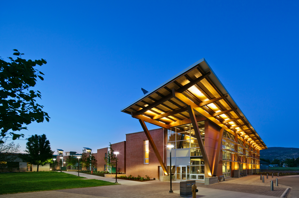 Exterior evening image of Okanagan College Centre Of Excellence showing glue-laminated timber (glulam) beams which support main atrium as a part of this net-zero centre for sustainable building technologies and renewable energy conservation