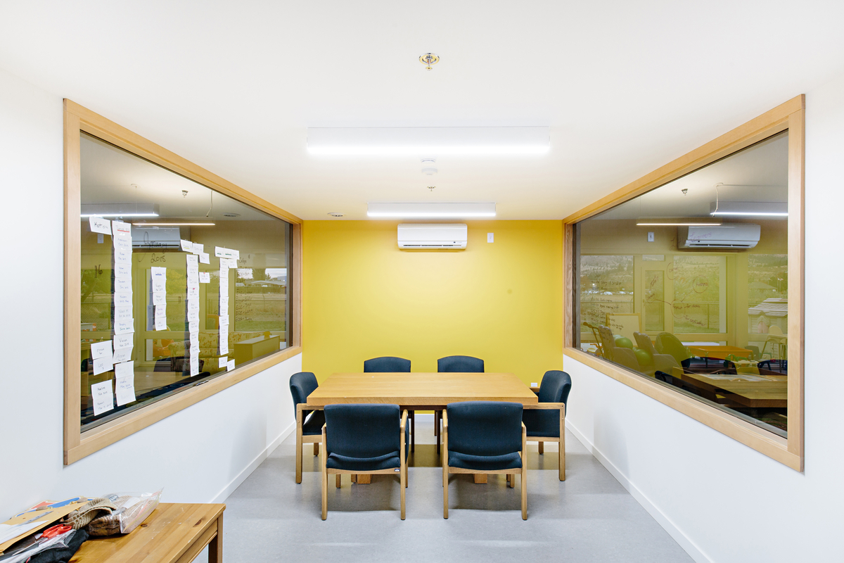 Interior sunny daytime view of low rise Okanagan College Child Care Centre meeting room with six chairs around a rectangular table, showing light frame and mass timber construction, including wooden trim