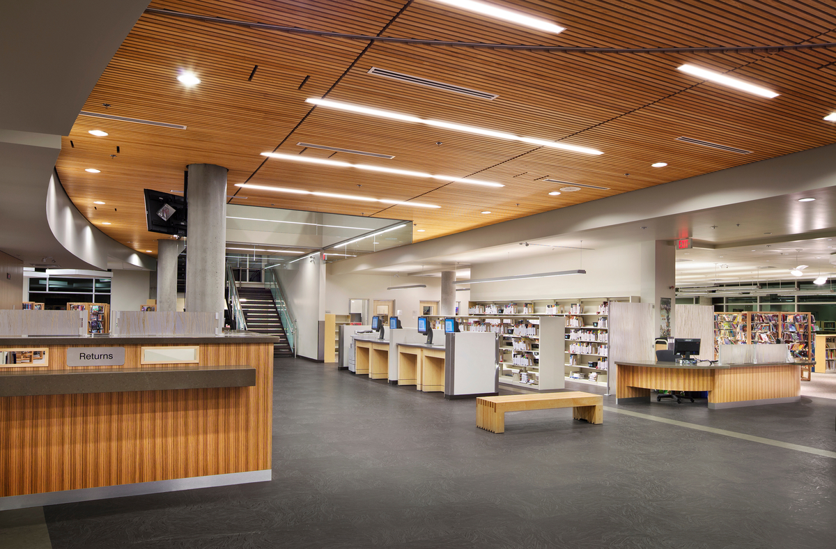 Interior daytime view of Okanagan Regional Library showing slatted wood ceilings which reduce ambient noise and millwork & veneers, which add to the richness and warmth of the space