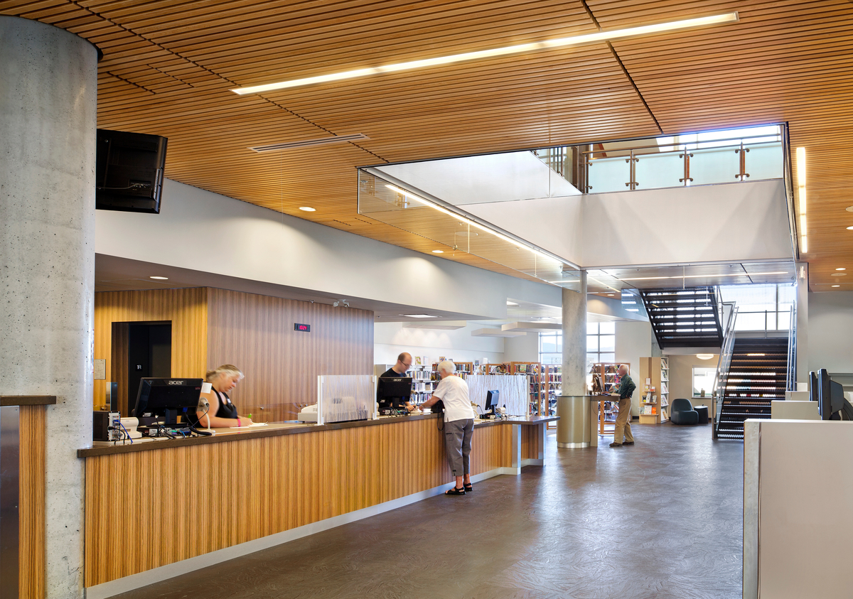 Interior daytime view of Okanagan Regional Library central area showing slatted wood ceilings which reduce ambient noise and millwork & veneers, which add to the richness and warmth of the space
