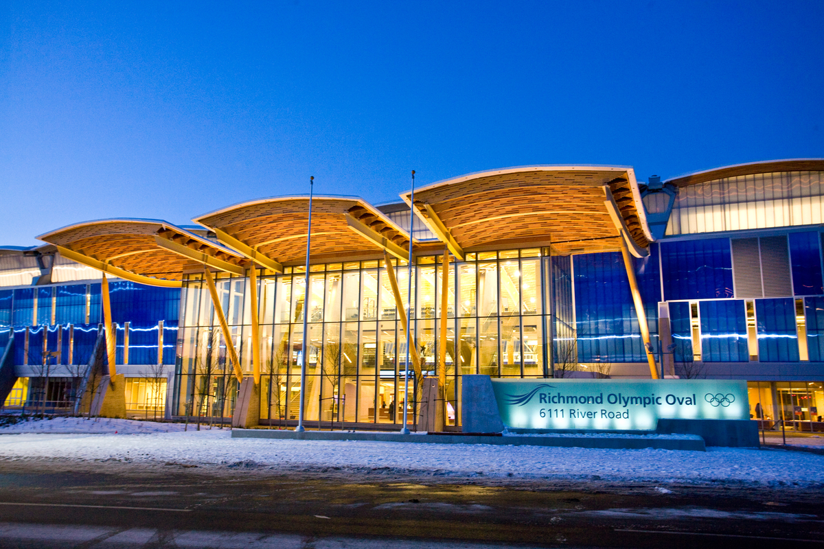Exterior evening image of glue-laminated timber (Glulam), solid-sawn heavy timber, and wooden accents as featured in the expansive exterior entrance roof of the 33,750 square meter Richmond Olympic Oval