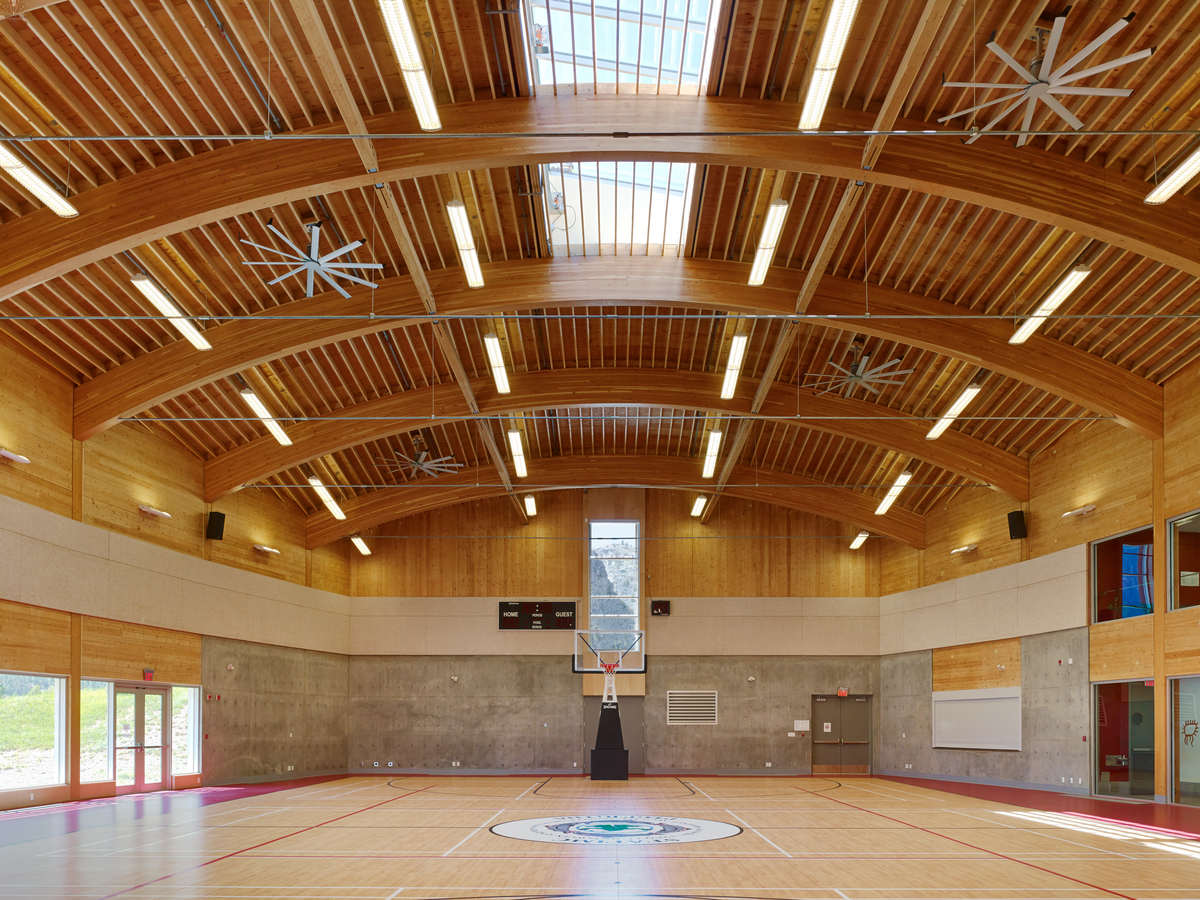 Interior daytime view of two storey P’Egp’Ig’Lha Community Centre gymnasium showing full span arching glue-laminated timber (Glulam) beams supporting dimensional lumber rafters and plywood sheathing