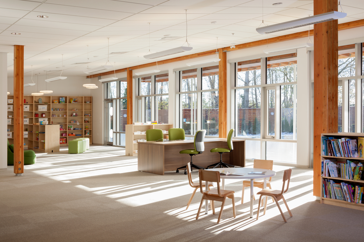 Bright sunny interior view of Pacific Autism Family Centre activity room, showing exterior glass windows, and interior wood which includes glue-laminated timber (glulam) beams and columns, wood cabinets, and wood trim