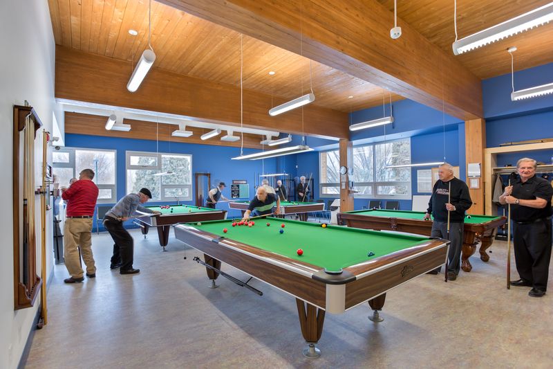 Interior of Parkinson Activity Centre with people socializing and playing pool in a well lit room with large wood beams and wood ceiling accents