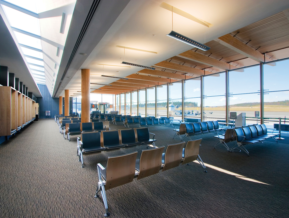 Interior daytime view of low rise Prince George Airport Expansion showing blue chairs, sculpted ceiling and structural post + beam timbers supporting Glue-laminated timber (Glulam)
