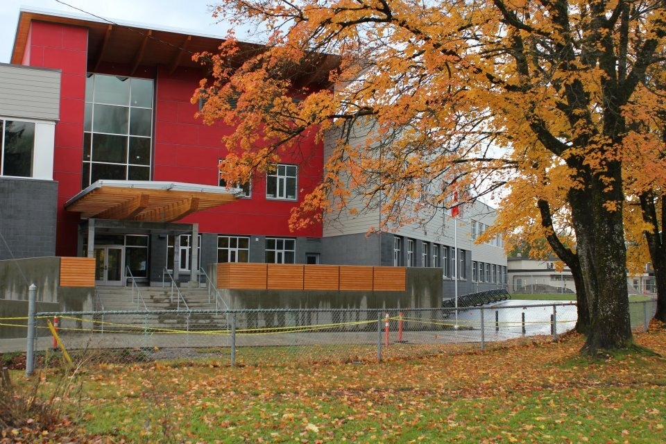 Exterior rainy fall daytime view of Revelstoke Secondary School and Begbie View Elementary School showing glue-laminated timber (glulam), dimensional lumber, and metal main entry roof; above concrete stairs