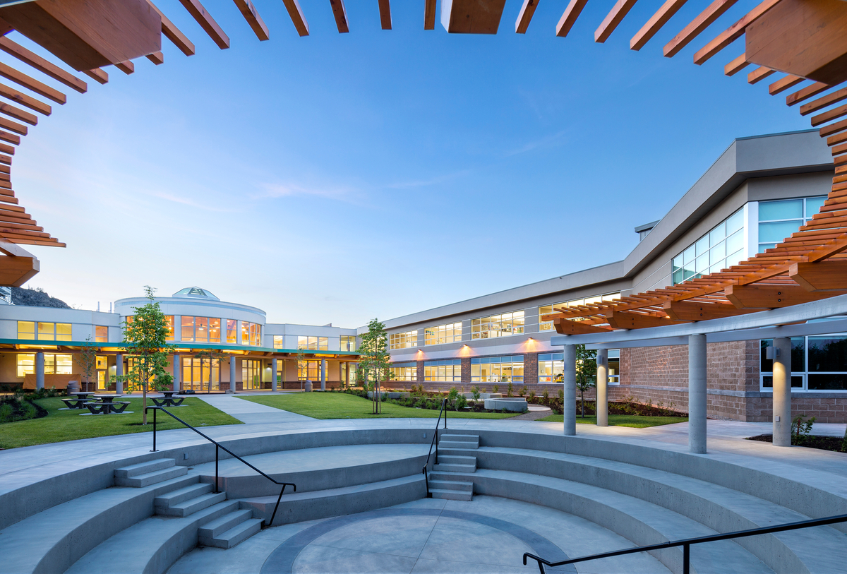 Exterior early evening view of Southern Okanagan Secondary School, highlighting circular wood arbor consisting of glue-laminated timber (Glulam) beams supporting dimensional lumber rails with dimensional lumber slats on edge above