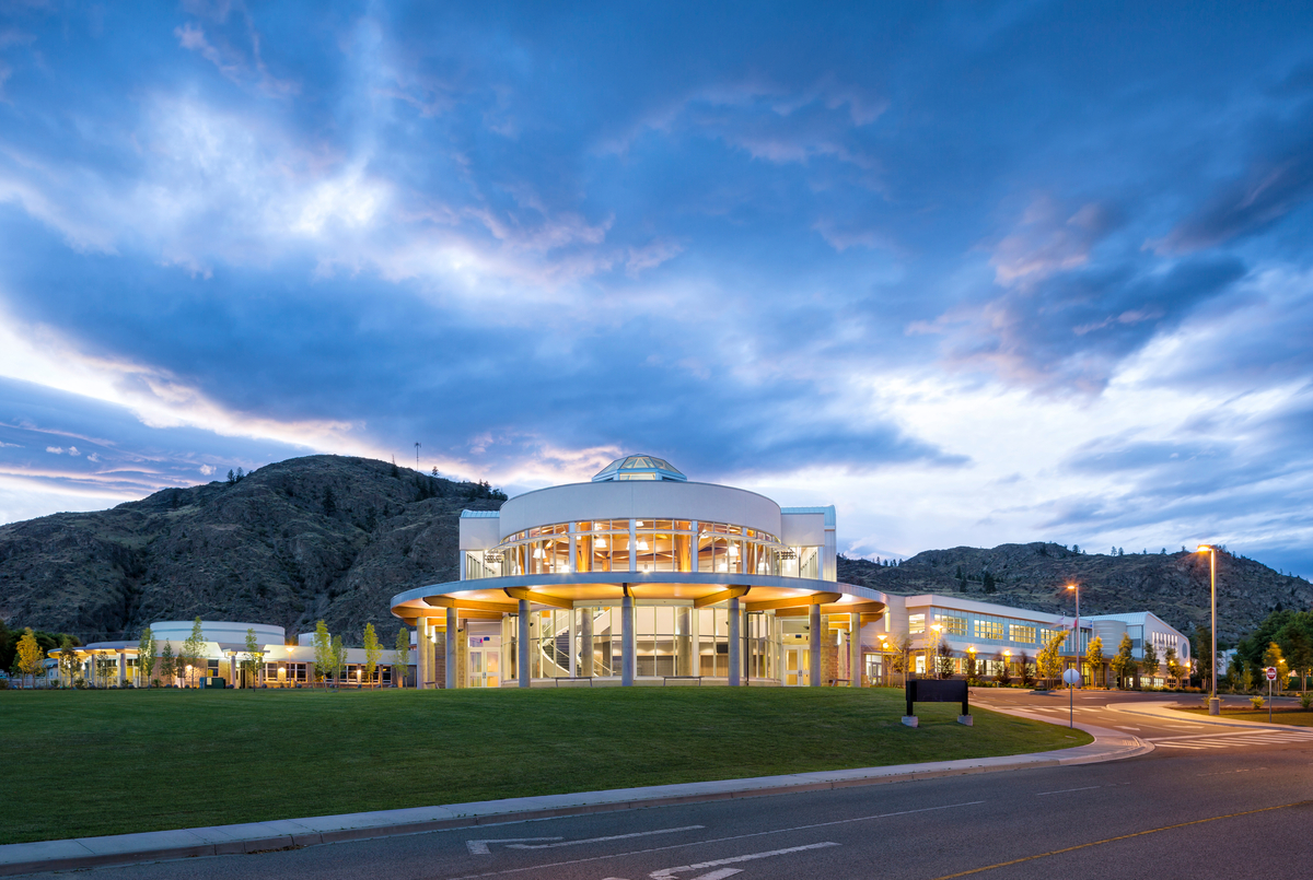Exterior early evening view of Southern Okanagan Secondary School, showing large circular main building with glue-laminated timber (Glulam) beams inside