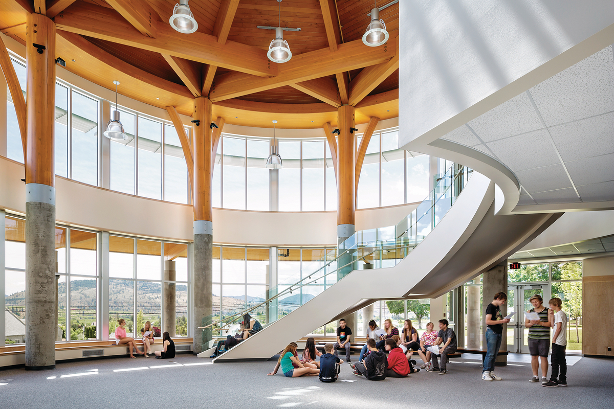 Interior daytime image showing the mass timber ceiling of the Southern Okanagan Secondary School three storey atrium, including massive post and beam supports atop concrete pedestals, supporting glue-laminated timbers and other mass timber ceiling elements