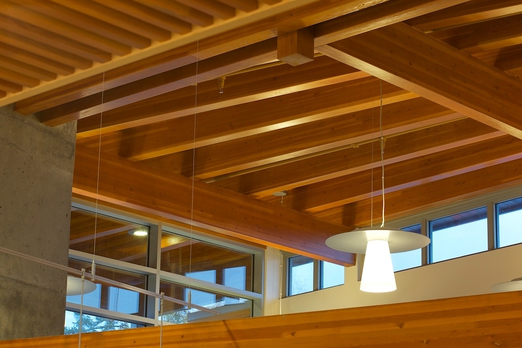 Interior upward close up daytime view of Salt Spring Island Library ceiling structure, showing glue-laminated timber rafters as a component of acoustic linear wood ceilings, which muffle noise to help preserve a quiet, peaceful atmosphere