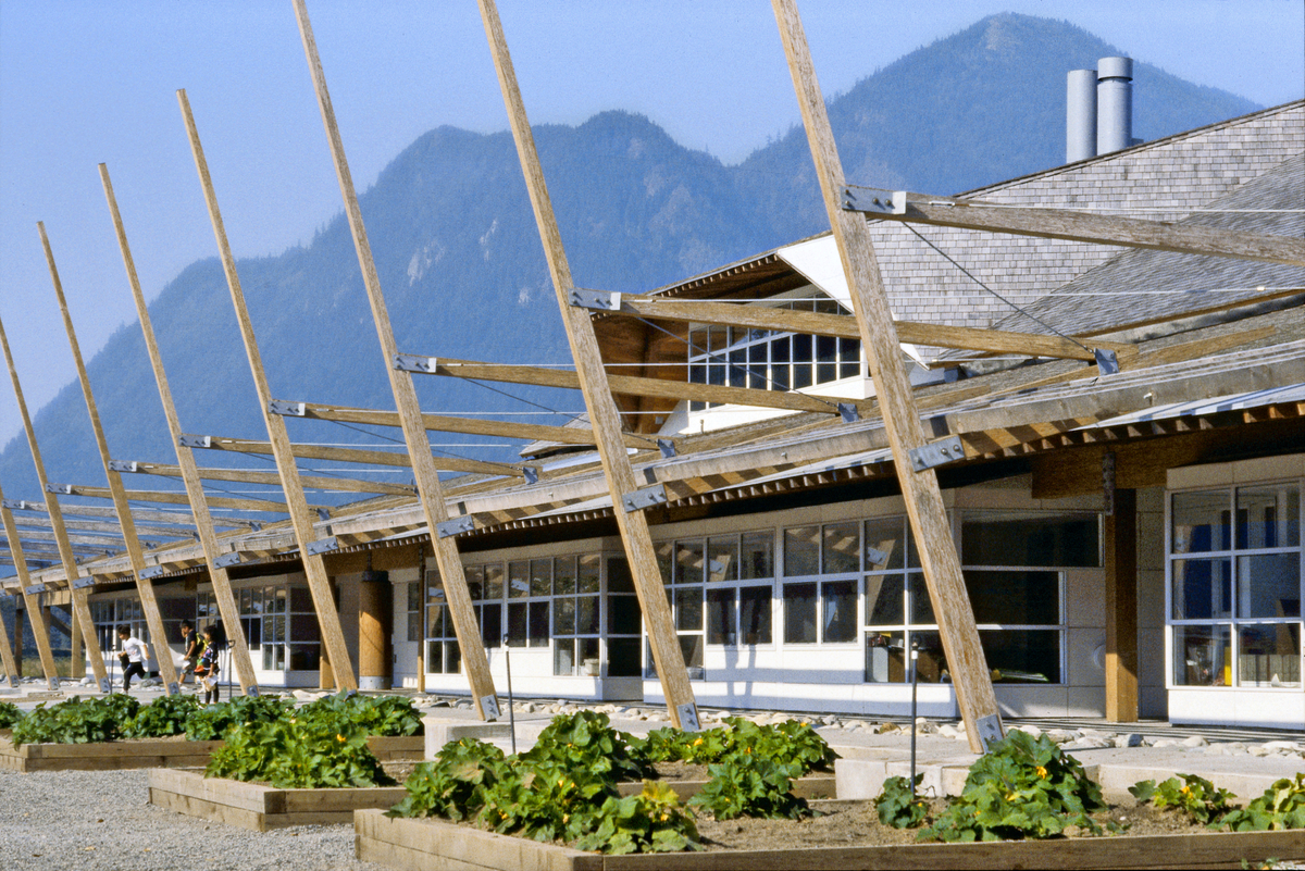 Sunny exterior ground level view of low rise Seabird Island Community School showing extensive use of lumber, plywood, siding, solid-sawn heavy timber, and post + beam construction