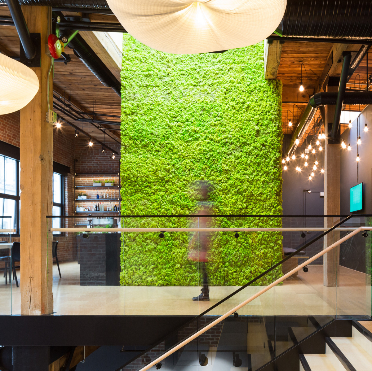 Interior daytime view of Slack Headquarters, showing century-old timber post-and-beam construction with massive timber beams and columns along with modern millwork and trim. Central to image is a natural green wall, made of lichen