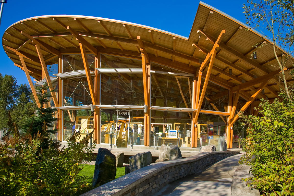 Exterior close up view of low rise hybrid Squamish Adventure Centre showing building’s signature upward angled curved wing-like roof represents the eagles in the Squamish Valley atop fully glazed exterior walls