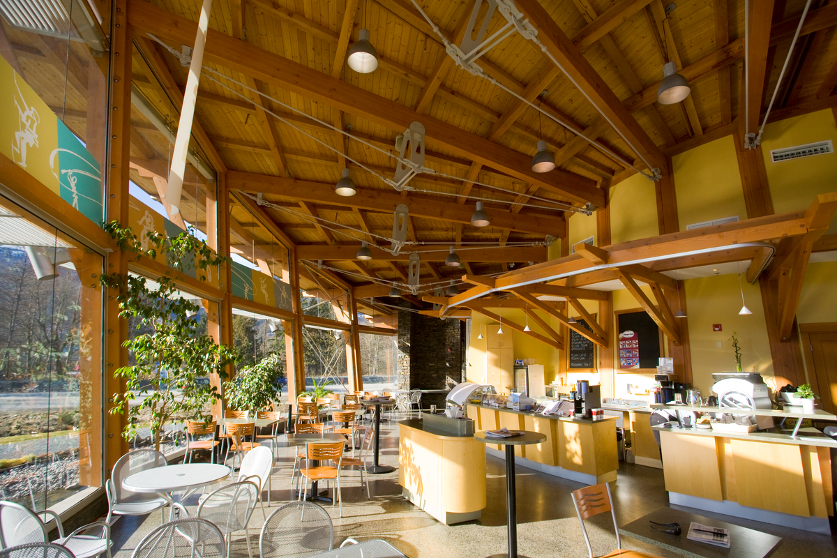 Interior view of Squamish Adventure Centre restaurant showing a roof of solid-sawn heavy timber beams supporting timber trusses and dimensional lumber roof slats; all above glazed outer wall and brightly lit eating area
