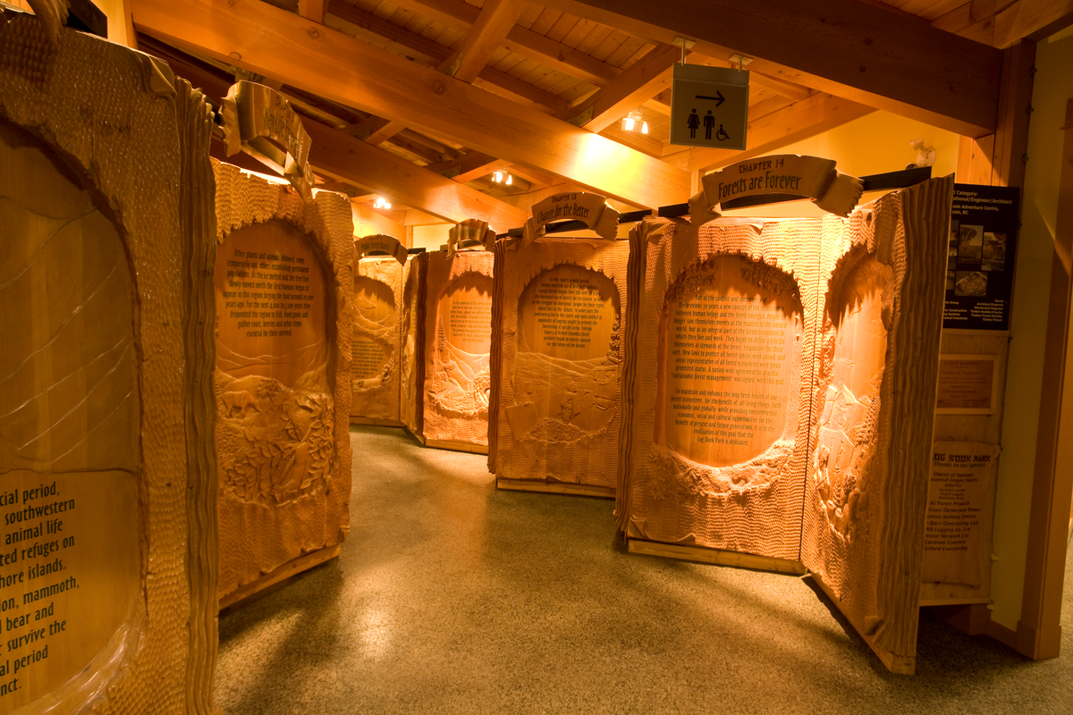 Interior view of Squamish Adventure Centre showing a roof of solid-sawn heavy timber beams supporting timber trusses and dimensional lumber roof slats; all above 2 meter high CNC carved 'books'