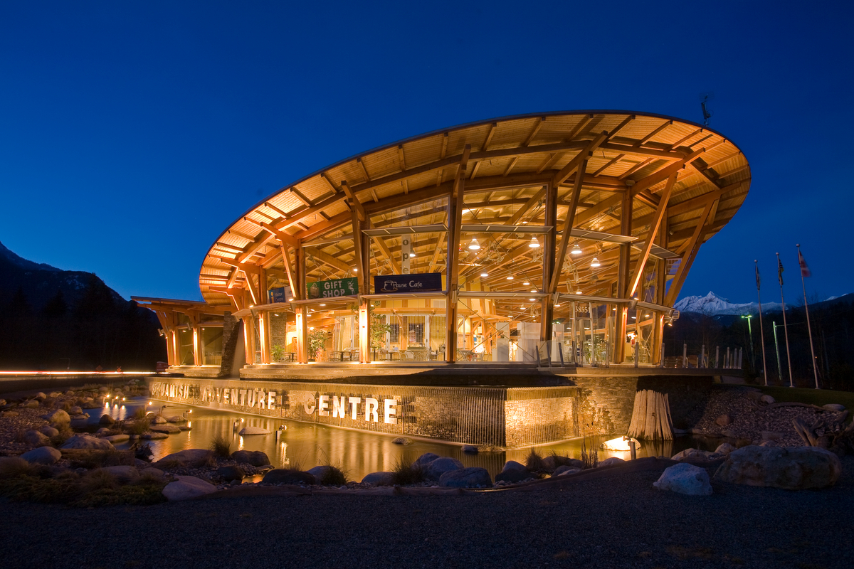 The low rise Squamish Adventure Centre, complete with curved wing-like roof and complex geometries, was built with solid-sawn heavy timbers and glows warmly in this exterior evening view