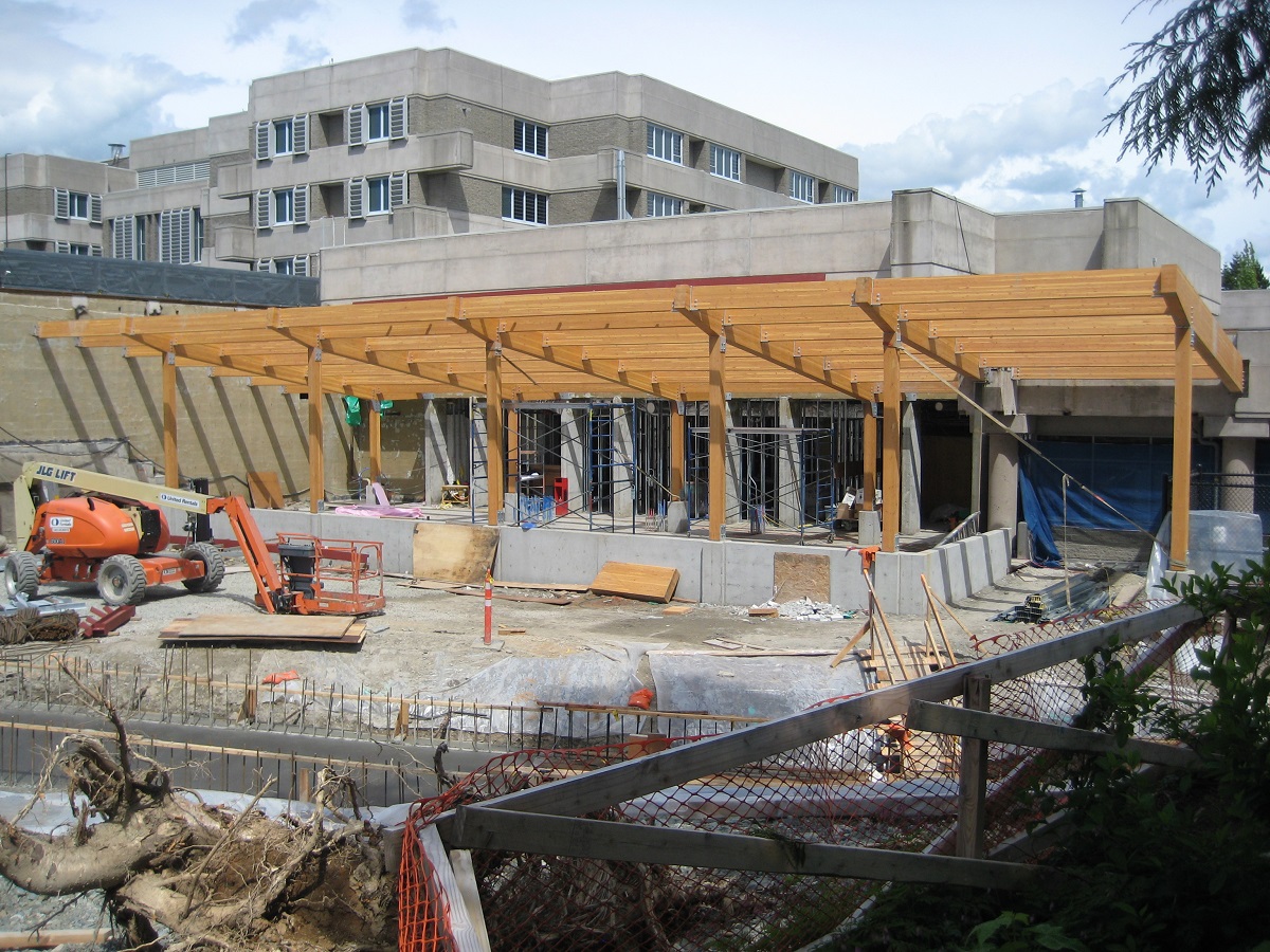 Exterior sunny early construction daytime view of close up of single story segment of Surrey Pretrial Services Centre showing various wood elements including a roof supported by glue-laminated timber (Glulam) beams and columns