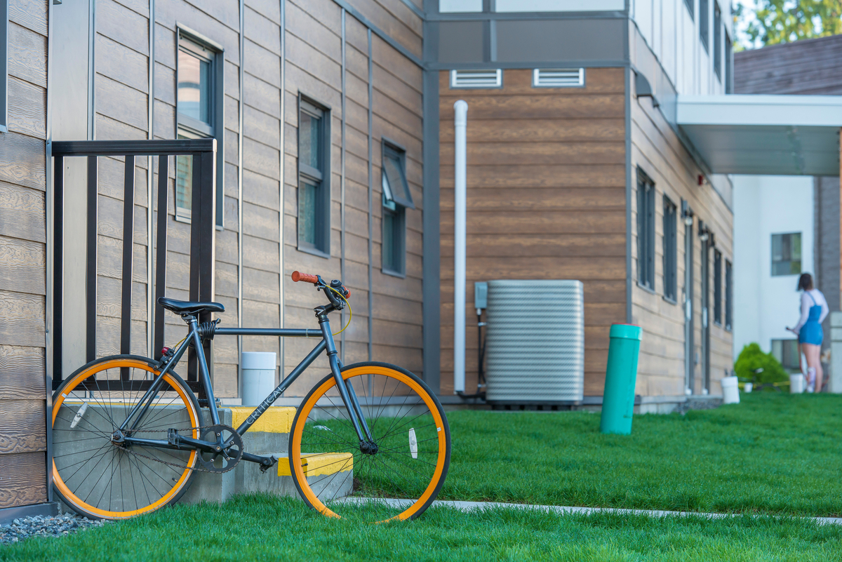 Exterior daytime view of Trinity Western University Jacobson Hall showing wood siding, windows, green grass, and a bicycle with orange wheels