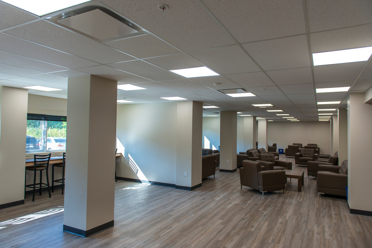 Interior view of Trinity Western University Jacobson Hall socialization area showing wooden flooring, brown lounge chairs, and sunshine entering through windows