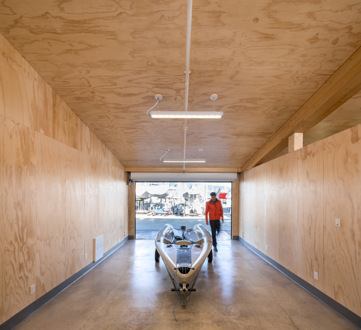 Interior daytime view of man and boat inside Dock Building at the Royal Vancouver Yacht Club, showing sunny interior storage area constructed from spruce-pine-fir glulam posts and beams with 2 x 6 Douglas-fir tongue and groove plywood infill decking