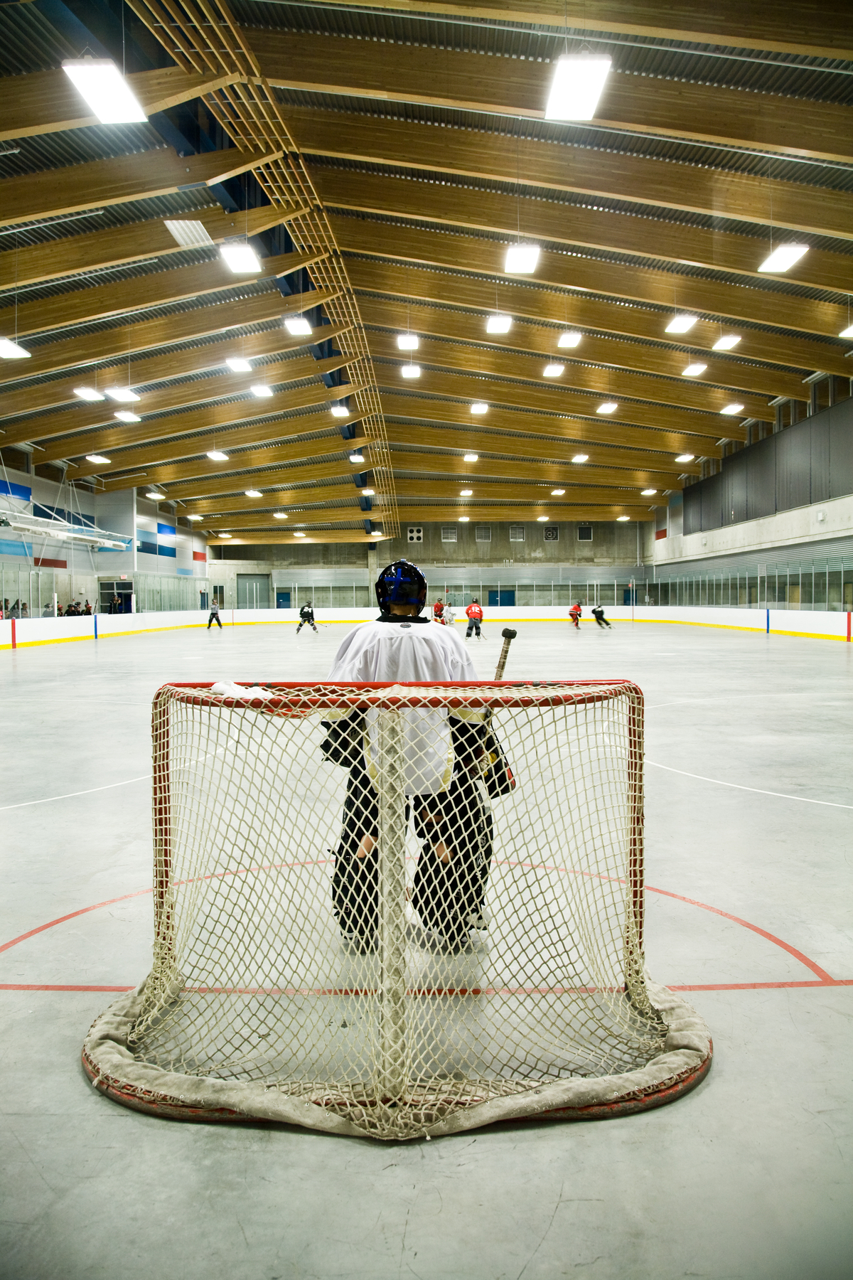 Interior view of Trout Lake Ice Rink showing hockey practice from perspective of goalie, all under the Glue-laminated timber (glulam) roof design which affords natural ventilation and lighting