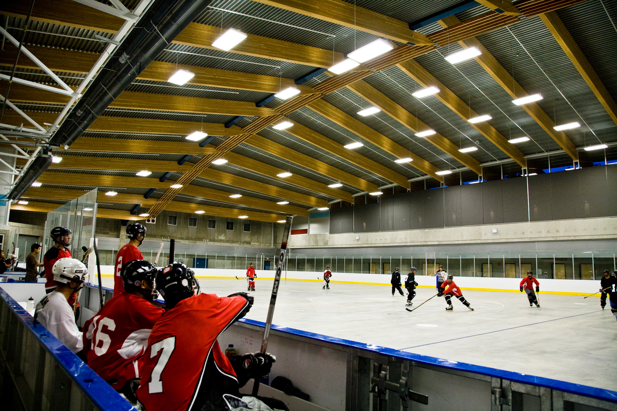 Interior occupied view of Trout Lake Ice Rink showing glue-laminated timber (glulam) roof design above ice rink with hockey players below