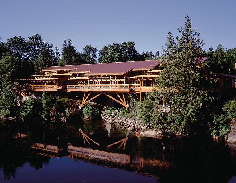 glue-laminated timber (glulam), millwork, paneling, and siding are all show in this sunny expansive exterior lakeside image of the Tseshaht Tribal Multiplex and Health Centre which highlights the abundant use of exterior wood for the column supports, wrap around balcony, window trim, roof trusses, eves, and more