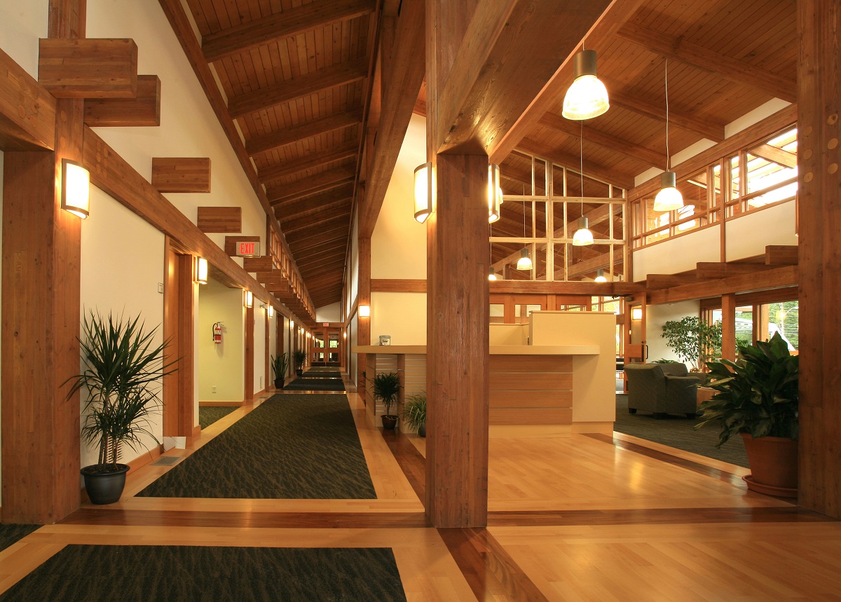 glue-laminated timber (glulam), millwork, and paneling are all show in this sunny interior image of the Tseshaht Tribal Multiplex and Health Centre which highlights the wooden floors, wooden ceilings, timber beams, and wood accents