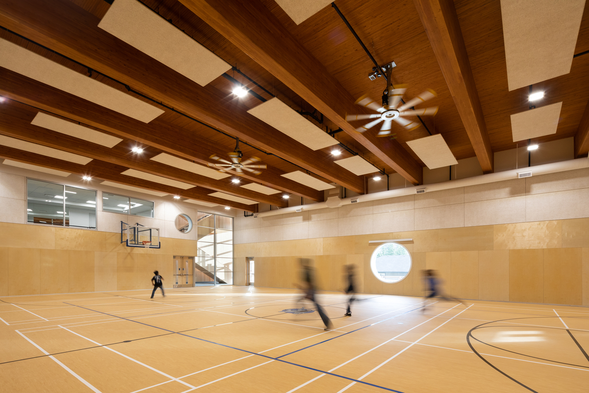 Interior view of Ts’kw’aylaxw Cultural and Community Health Centre gymnasium showing Glue-laminated timber (Glulam) and Nail-laminated timbers (NLT) during a pickup basketball game.