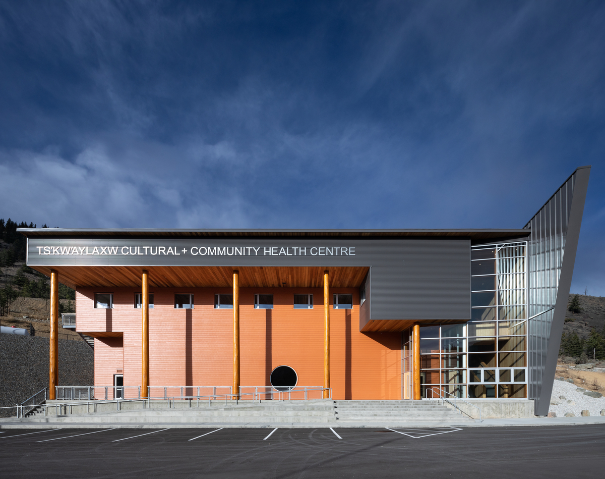 glue-laminated timber (glulam), lumber, millwork, nail-laminated timber (nlt), and paneling, are all featured in this exterior daytime image of the Ts’kw’aylaxw Cultural and Community Health Centre which highlights the mass timber, passive house / high performance construction of this building
