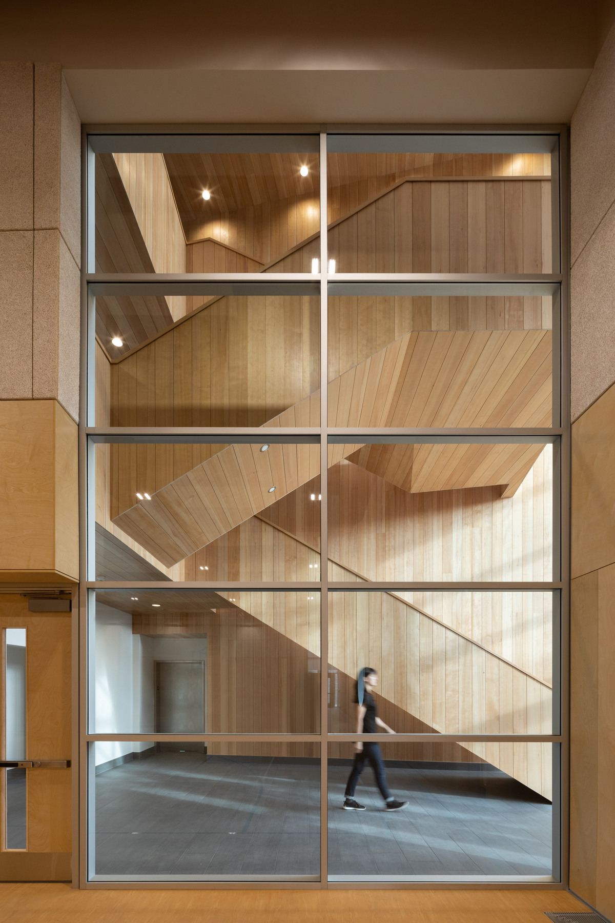 glue-laminated timber (glulam), lumber, millwork, nail-laminated timber (nlt), and paneling, are all featured in this interior daytime image of the Ts’kw’aylaxw Cultural and Community Health Centre which highlights the multi storey wooden switchback staircase