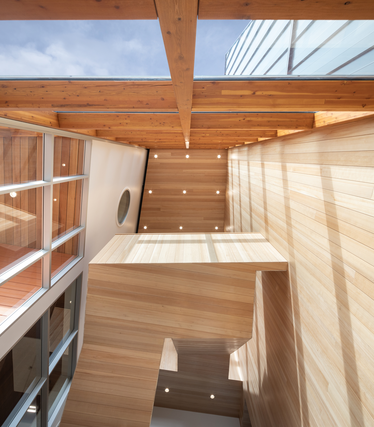 glue-laminated timber (glulam), lumber, millwork, nail-laminated timber (nlt), and paneling, are all featured in this interior upward vertical daytime image of the Ts’kw’aylaxw Cultural and Community Health Centre which highlights the multi storey wooden switchback staircase