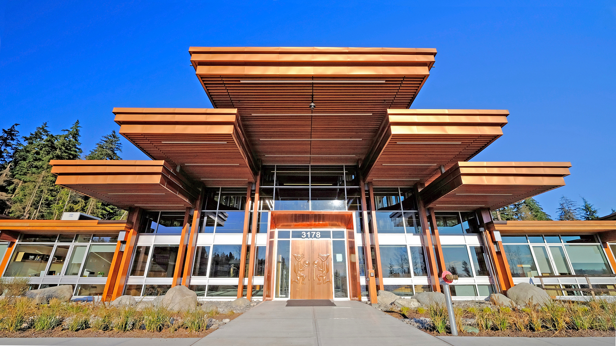 Exterior sunny daytime view of multi layered cantilever wooden roof sections extending out from Tsleil Waututh Administration and Health Centre