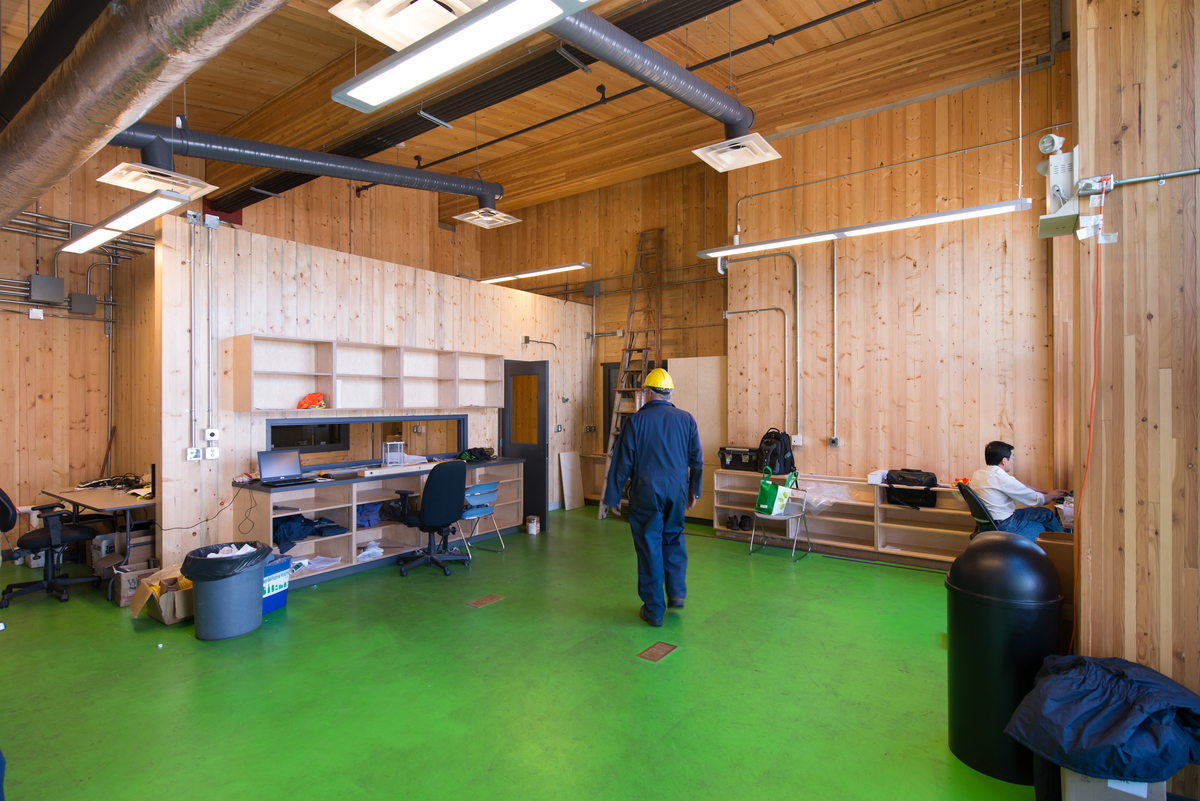 Interior daytime view of low rise mass timber constructed UBC Bioenergy Research and Demo Facility showing staff in a room surrounded by cross-laminated timber (CLT) wood paneling walls, and ceilings supported by large glue-laminated timber (Glulam) beams