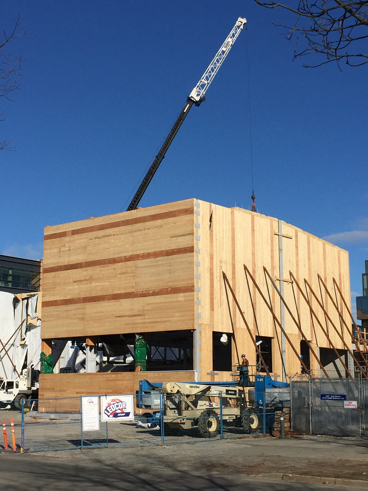 The UBC Campus Energy Centre primary structure, built from glue-laminated timber (glulam) post and beam frame, with cross-laminated timber (CLT) enclosed walls and roof, is shown in this sunny daytime early construction image with a crane