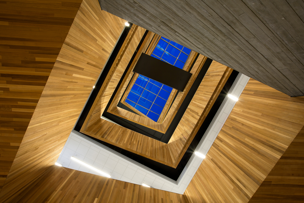 Multi storey upward stairwell interior image showing prominent use of exposed wood throughout the building, including wall cladding in the atriums, exposed wall guard protection and trim