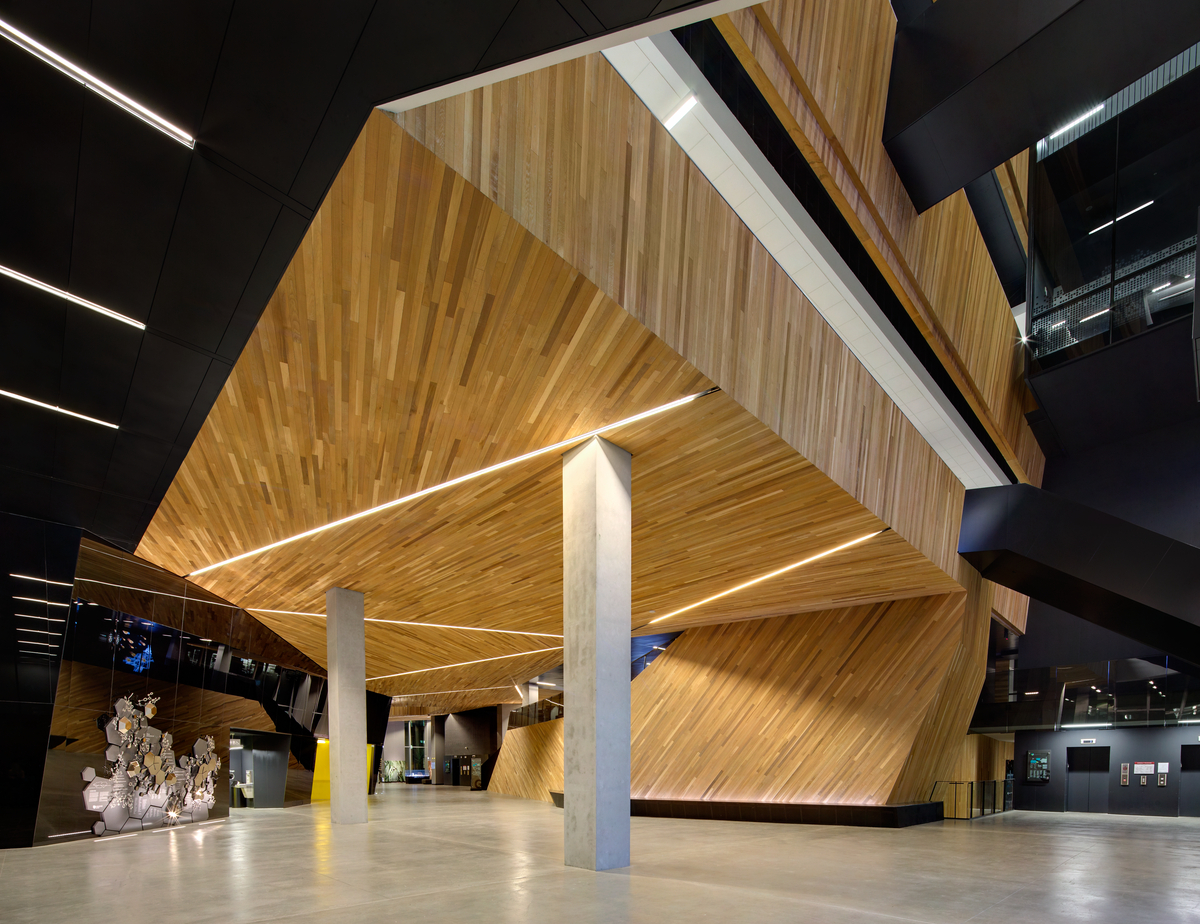 Interior evening view of UBC Pharmaceutical Sciences Building showing highly angular Western red cedar ceilings, concrete beams, and exposed wood and black detail