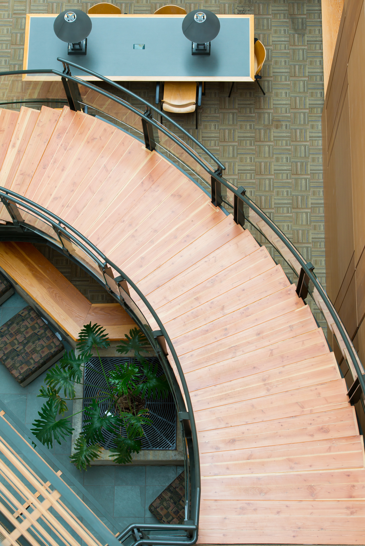 A large diameter circular stairwell with beautiful wood treads is shown in this downward view of the UBC Forest Sciences Centre main atrium