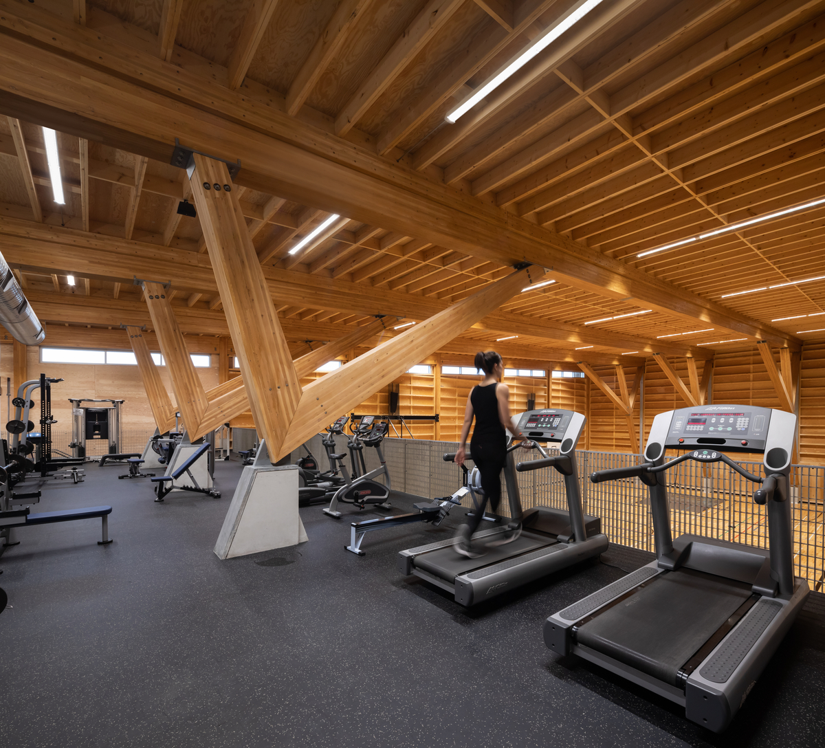 Full span glue laminated timber beams and columns support the roof in this interior view of the Upper Skeena Recreation Centre taken from the occupied 2nd floor exercise area