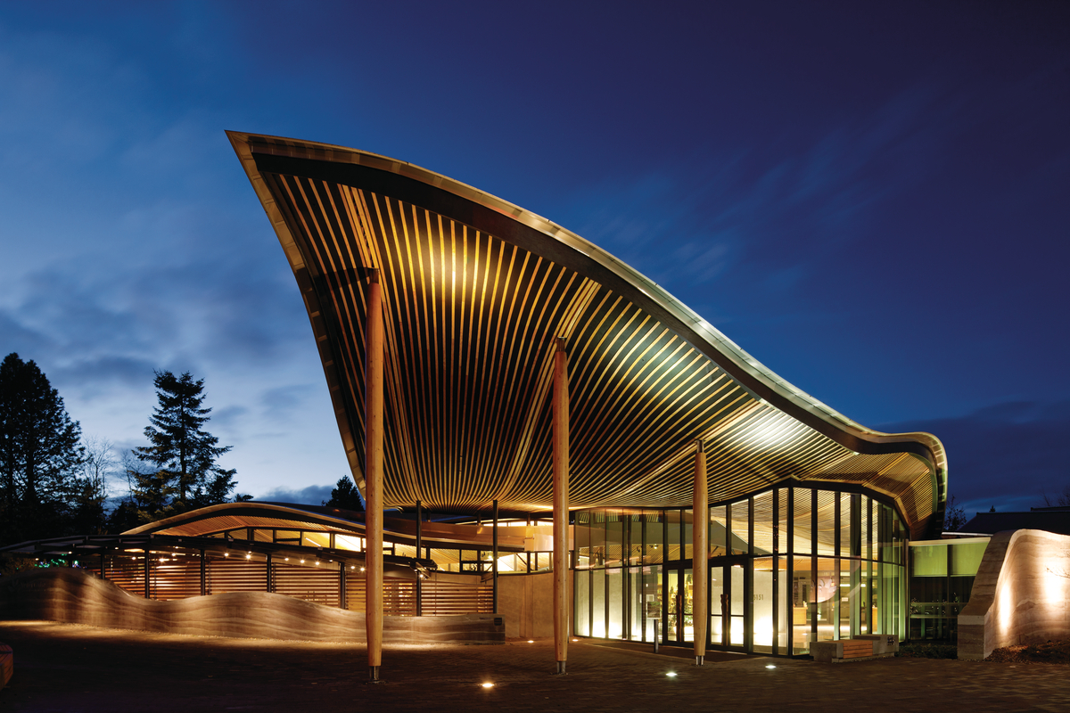 Exterior nighttime view of VanDusen Botanical Garden exterior covered entrance with swooping timber roof design made possible through precise prefabricated technology