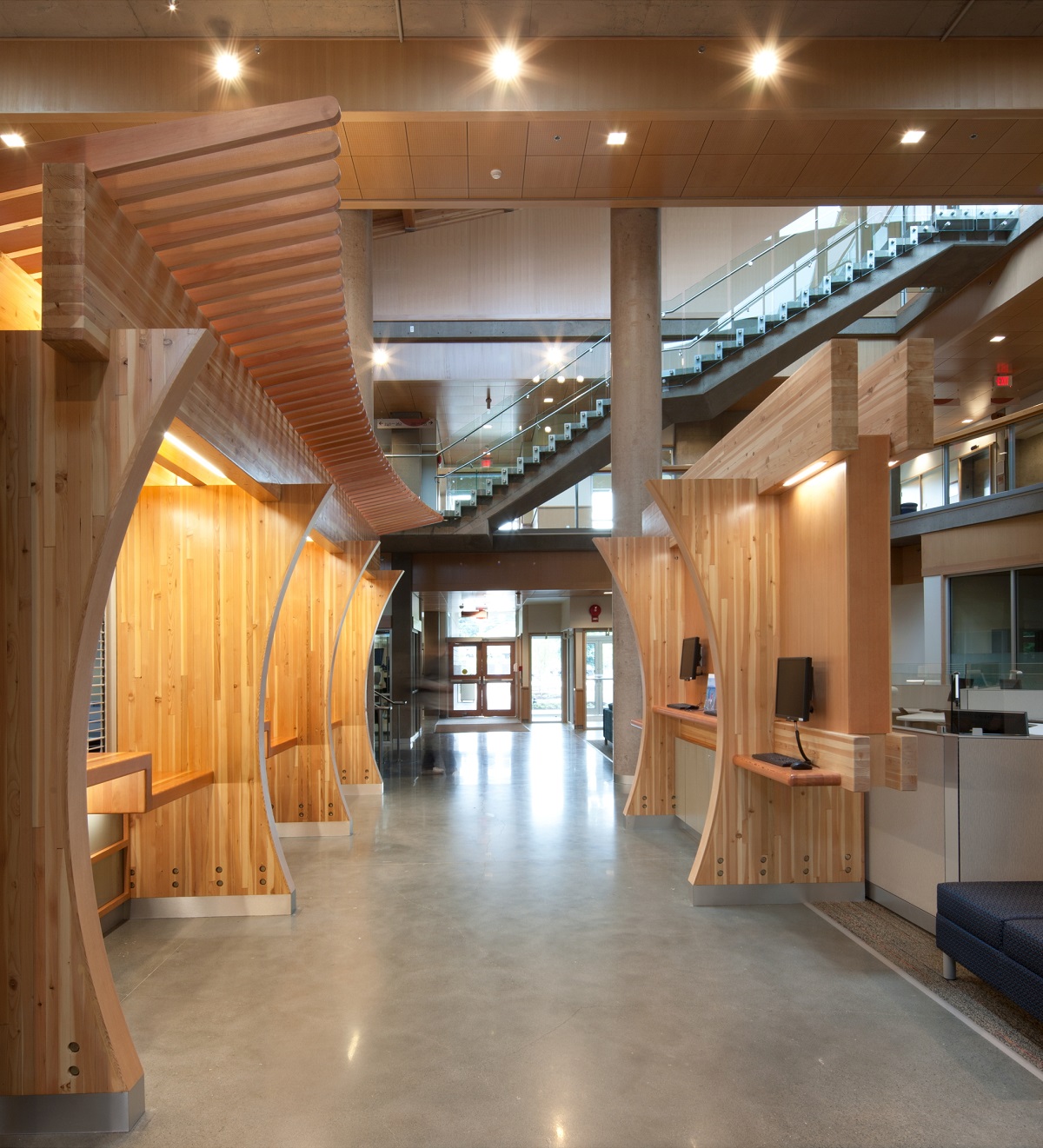 glue-laminated timber (Glulam) beams and decorative workstation dividers, wood trim, and decorative wood elements are all shown in this daytime interior image of the multi storey Vancouver Island University Cowichan Campus main entrance and atrium