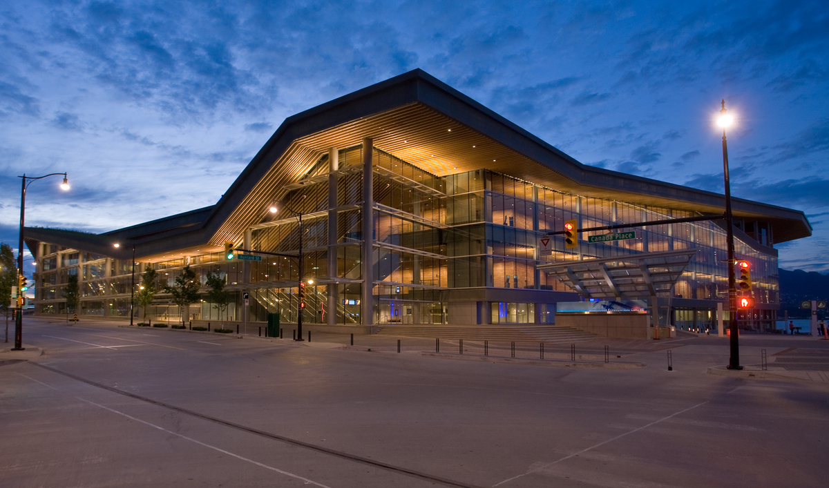 Exterior evening view of contemporary glass and wood fronted Vancouver Convention Centre West Building showing massive wooden roof structure topped by the largest “living roof” in Canada with 400,000 indigenous plants and grasses and four beehives
