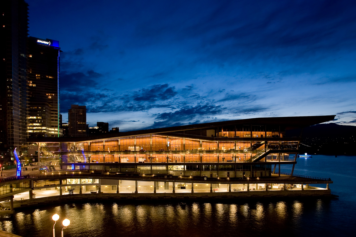 Exterior evening view of contemporary glass and wood fronted Vancouver Convention Centre West Building showing massive wooden roof structure topped by the largest “living roof” in Canada with 400,000 indigenous plants and grasses and four beehives