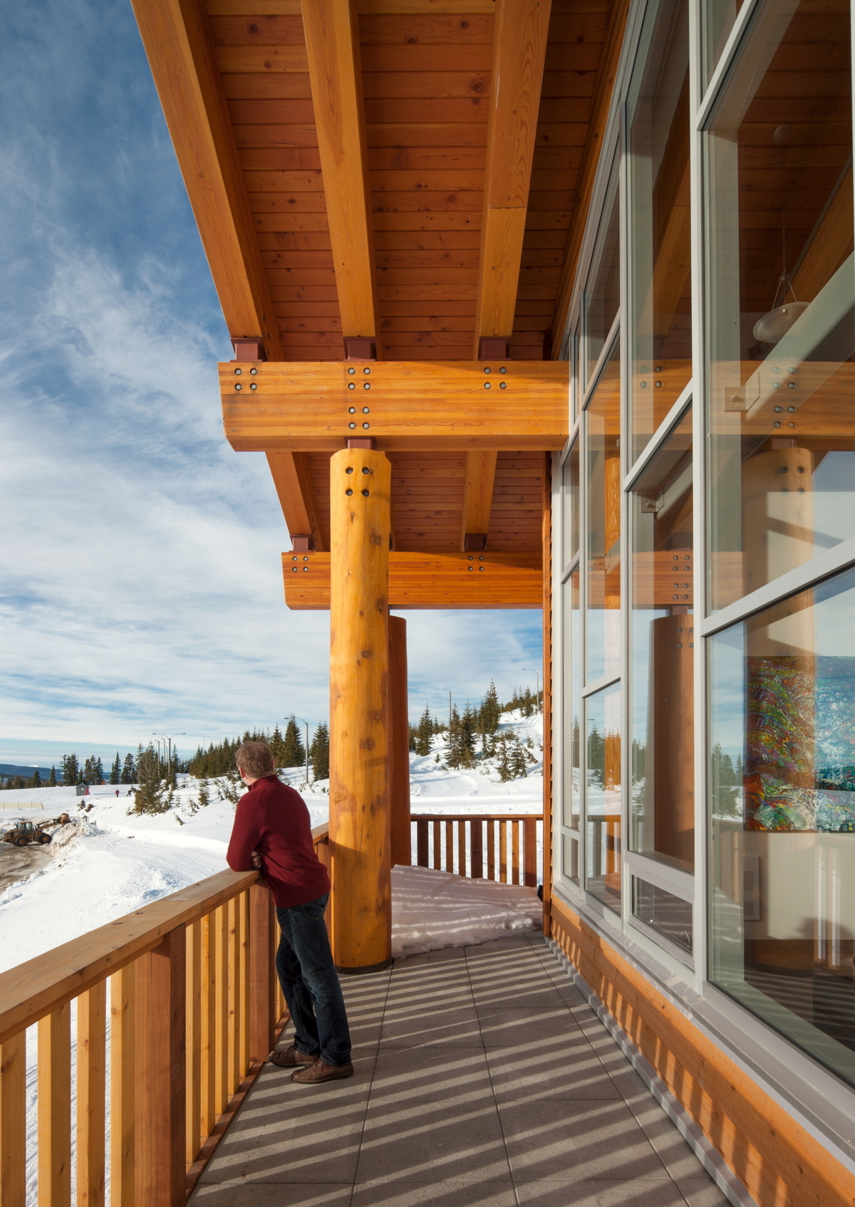glue-laminated timber (Glulam) beams, wood siding & soffit, solid-sawn heavy timber vertical pole columns, dimensional lumber banister & railing are all shown in this snowy sunny daytime image of the Vancouver Island Mountain Centre occupied external balcony