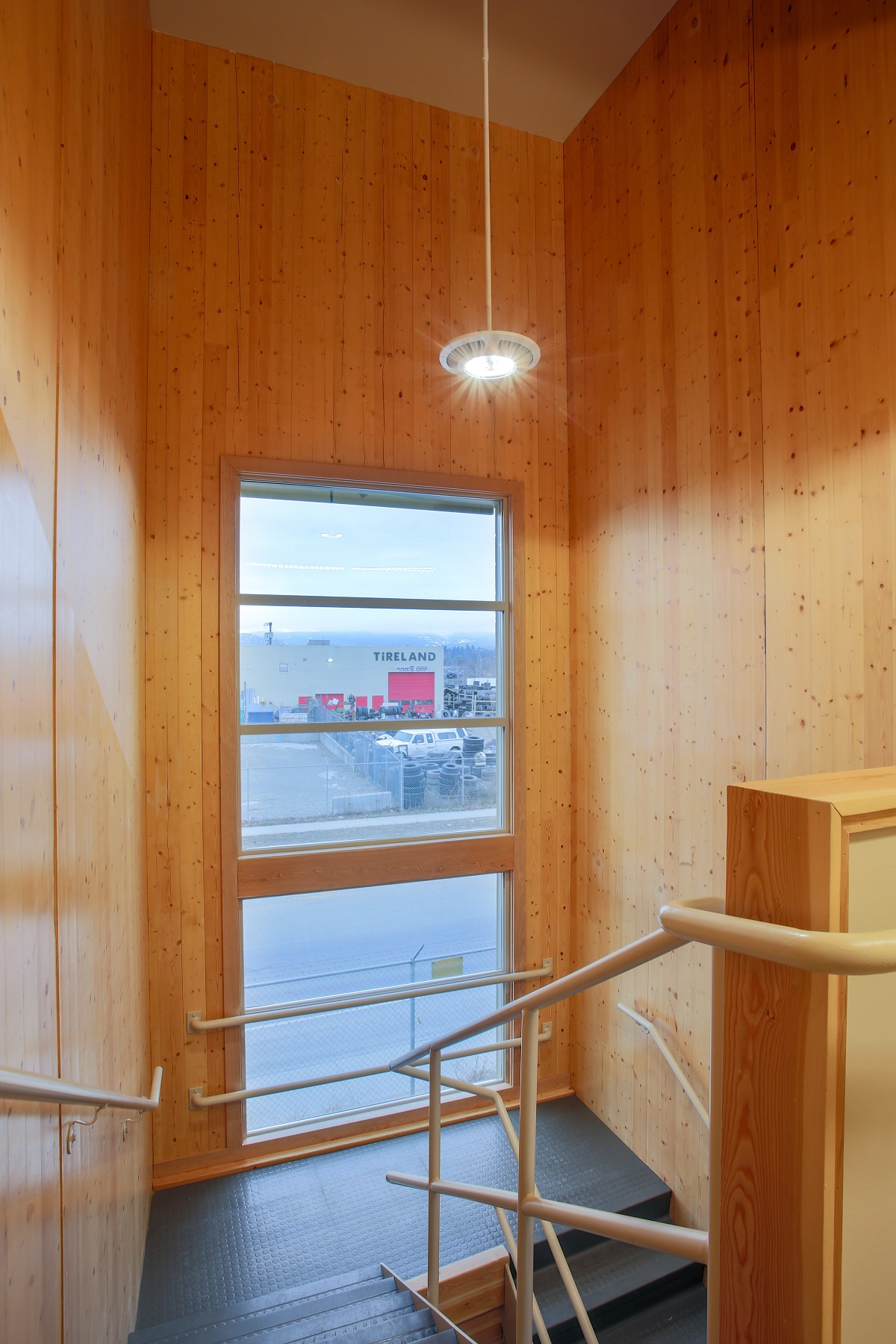 cross-laminated timber (CLT) wall panelling is showing is this brightly lit daytime top down image of the Van-Kam Freightways stairwell with large window and metal handrail